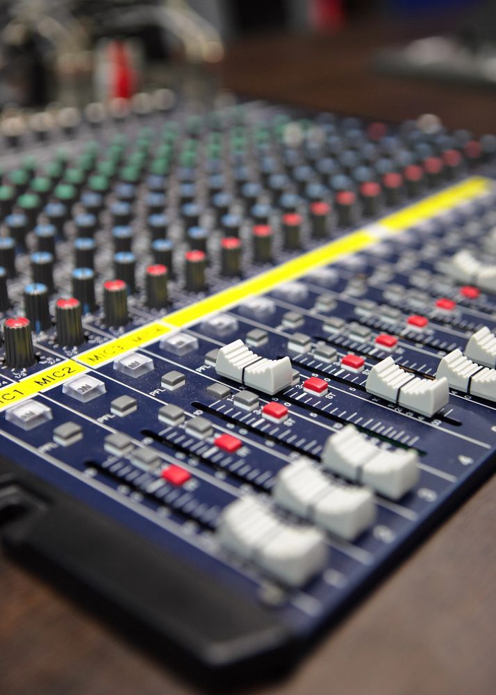 Console di mixaggio audio con manopole, fader e pulsanti, in blu scuro e dettagli colorati.