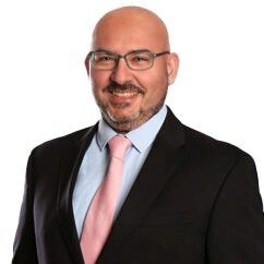 A man in a white coat and blue shirt smiles for the camera