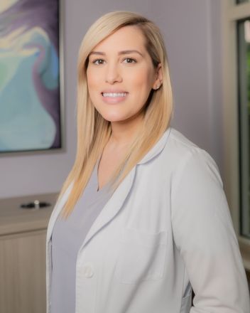 A woman in a lab coat is standing in front of a painting.