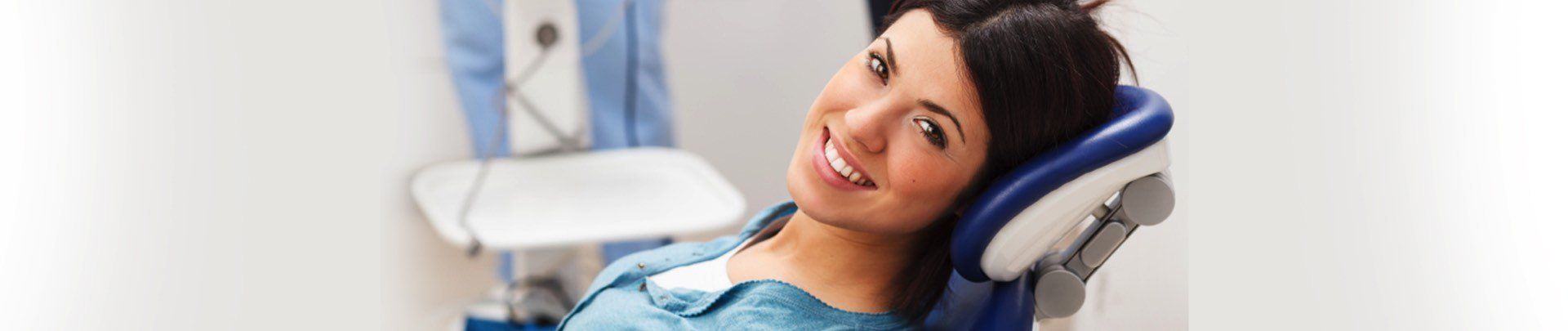 A woman is smiling while sitting in a dental chair.