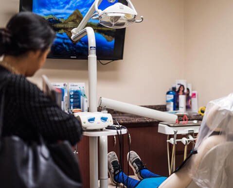 A woman is sitting in a dental chair looking at a tv.