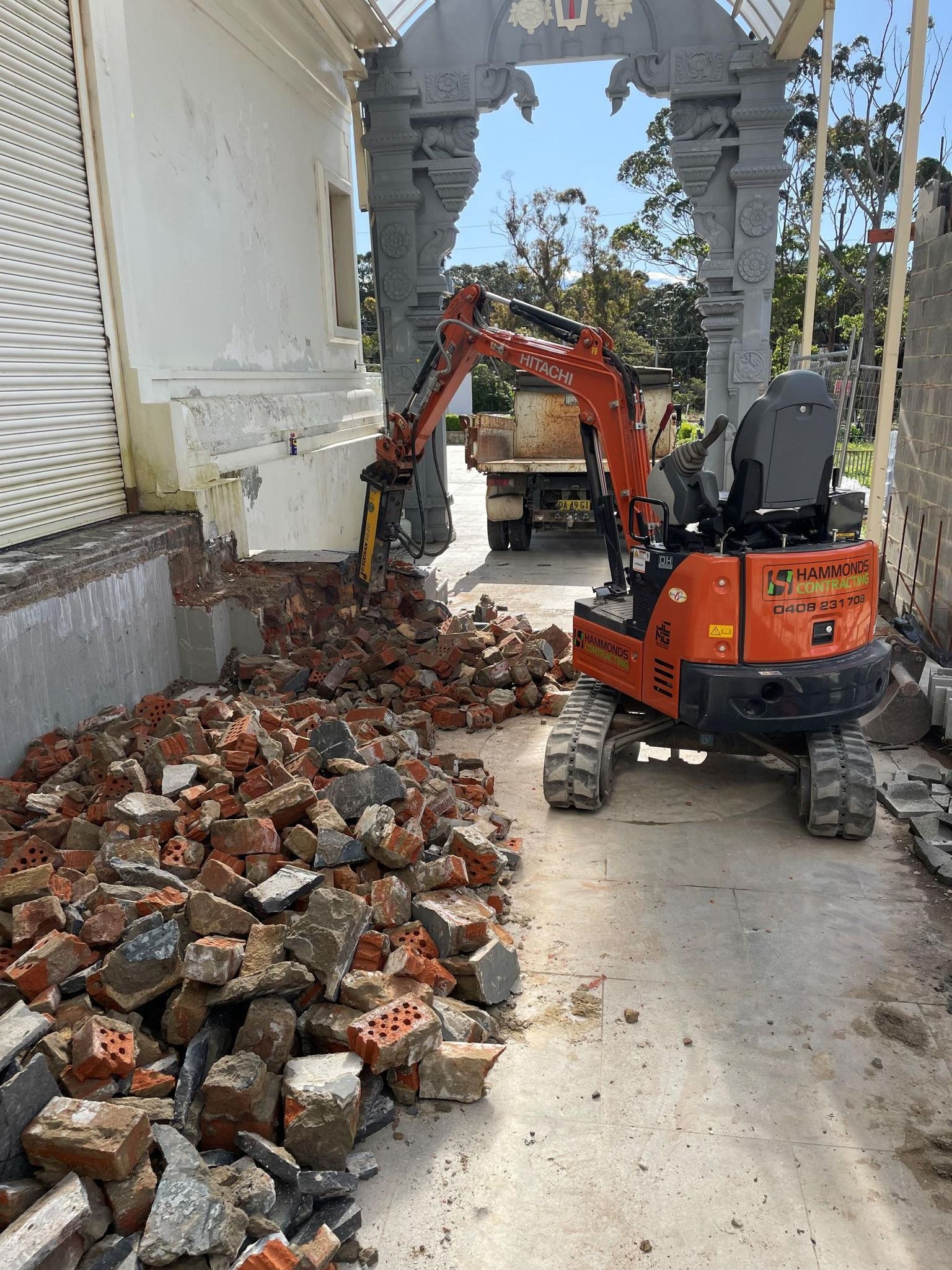 A small orange excavator is moving a pile of bricks.