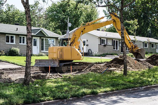 A yellow excavator is digging a hole in front of a house.