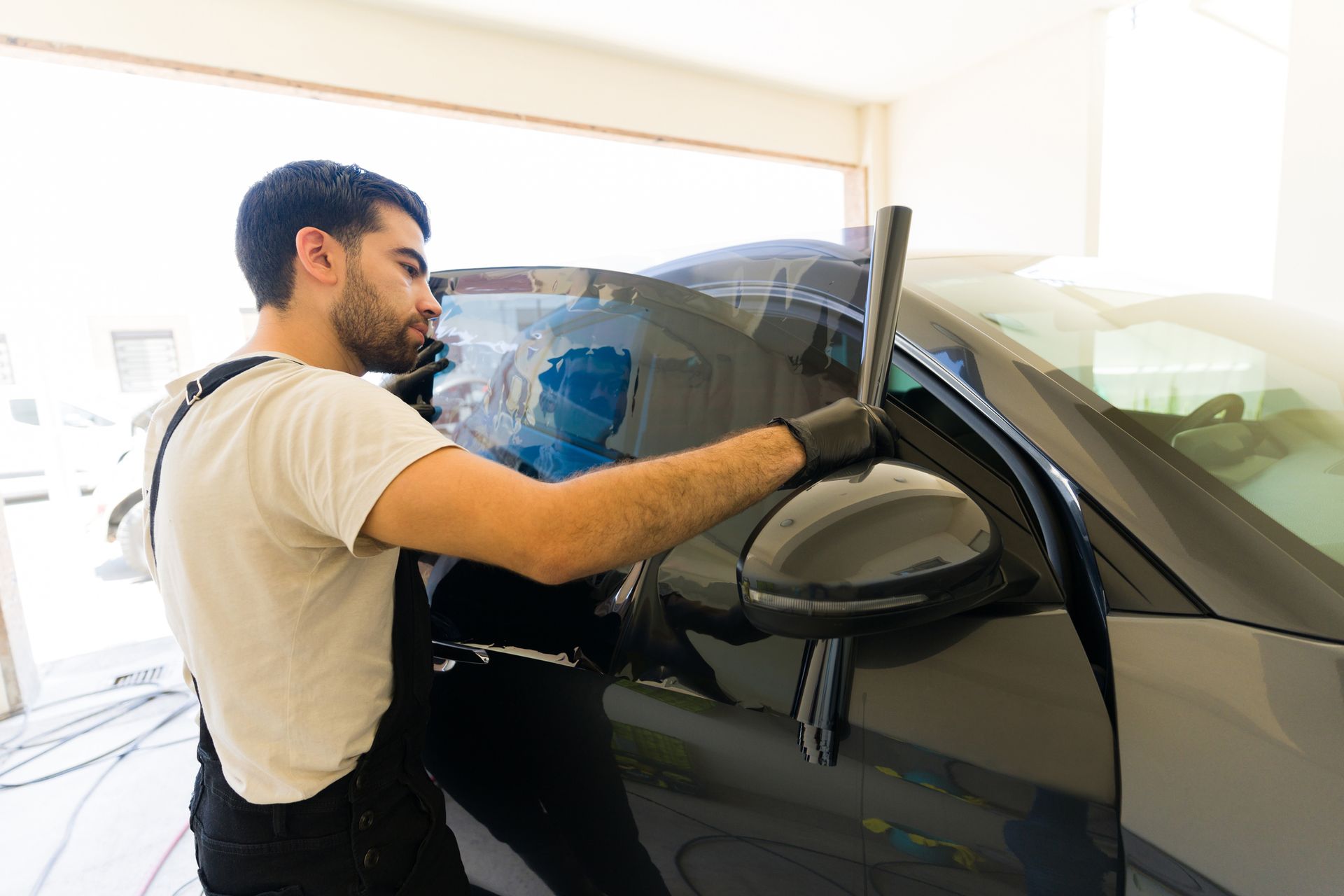 A man working at a car detail shop is measuring a tinting film of an auto window glass. A man working at a car detail shop is measuring a tinting film of an auto window glass.