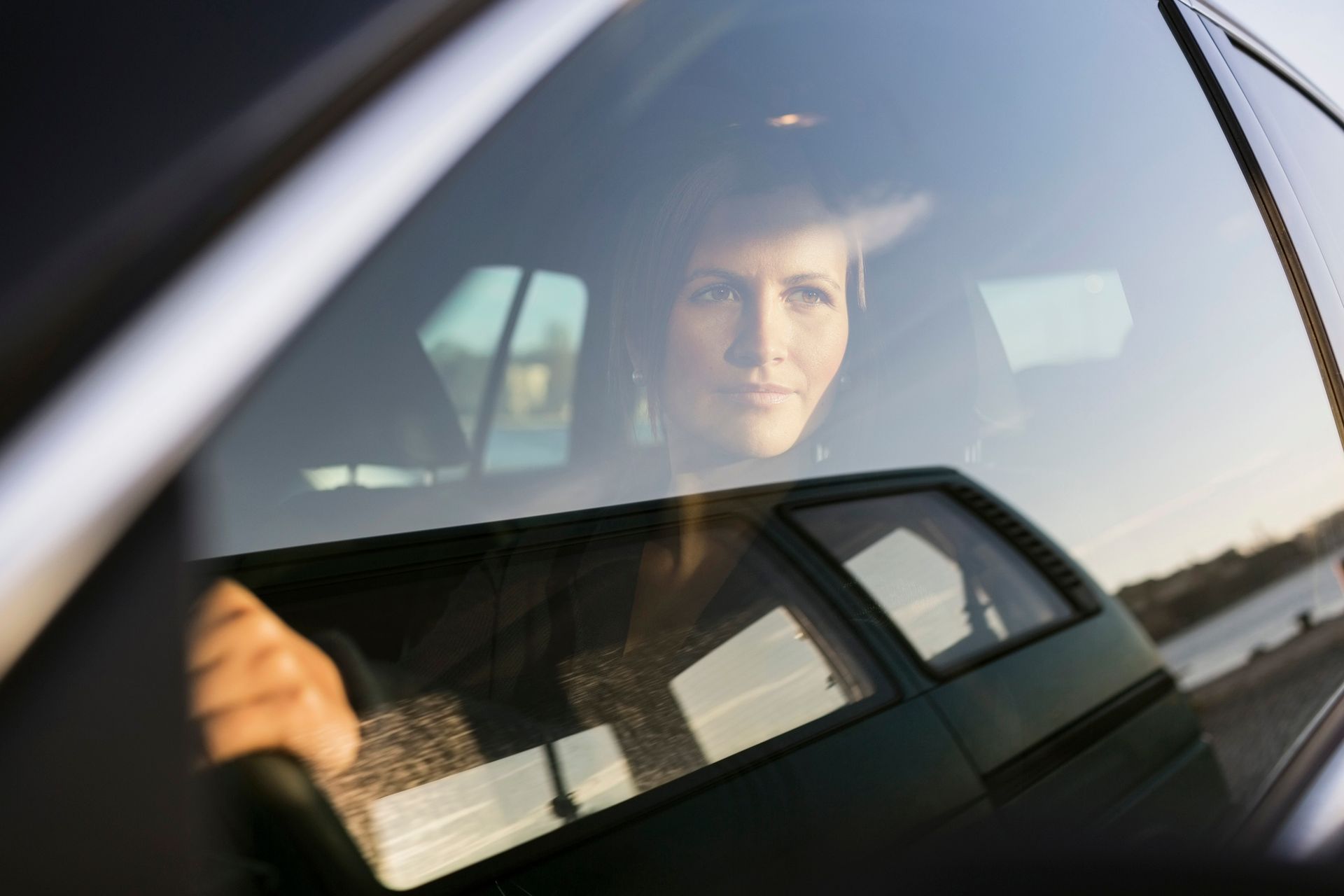 A woman looking through her driver’s side tinted window while she is driving.