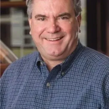 A man in a blue plaid shirt is smiling for the camera.