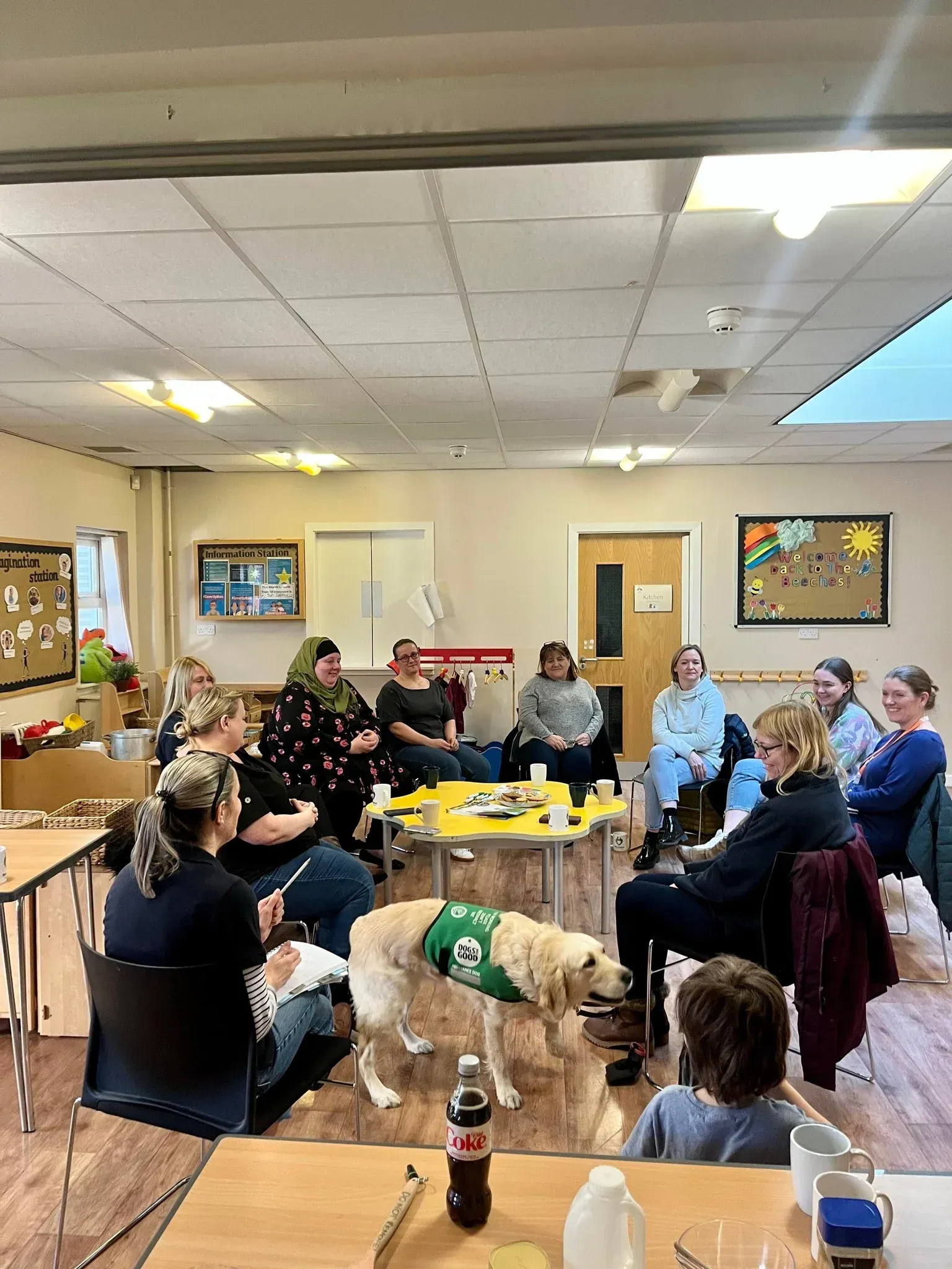 A group of people and a dog are sitting around a table in a room.