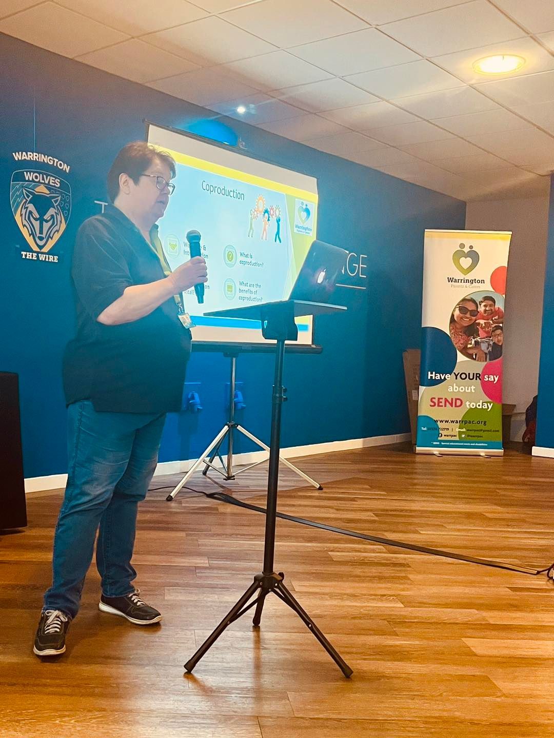 A man is standing in front of a projector screen holding a microphone.