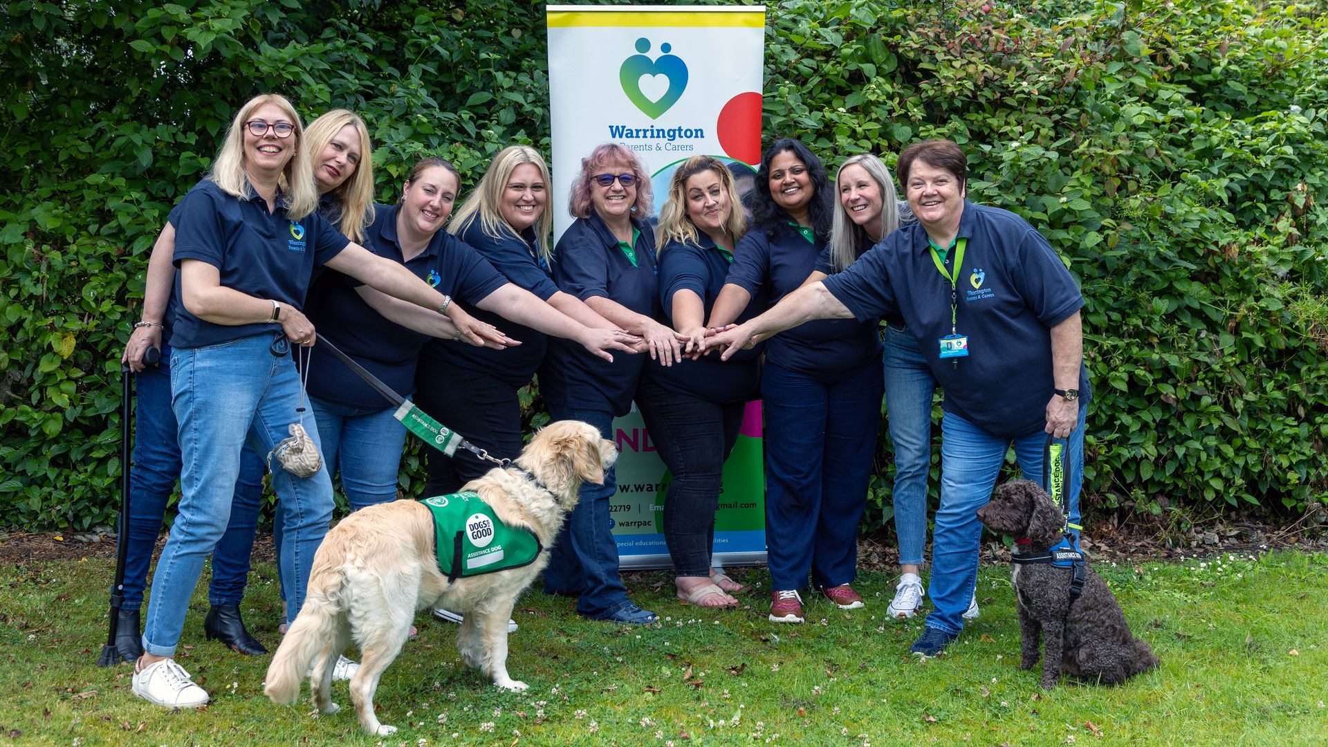 A group of women and a dog are standing next to each other in front of a sign.