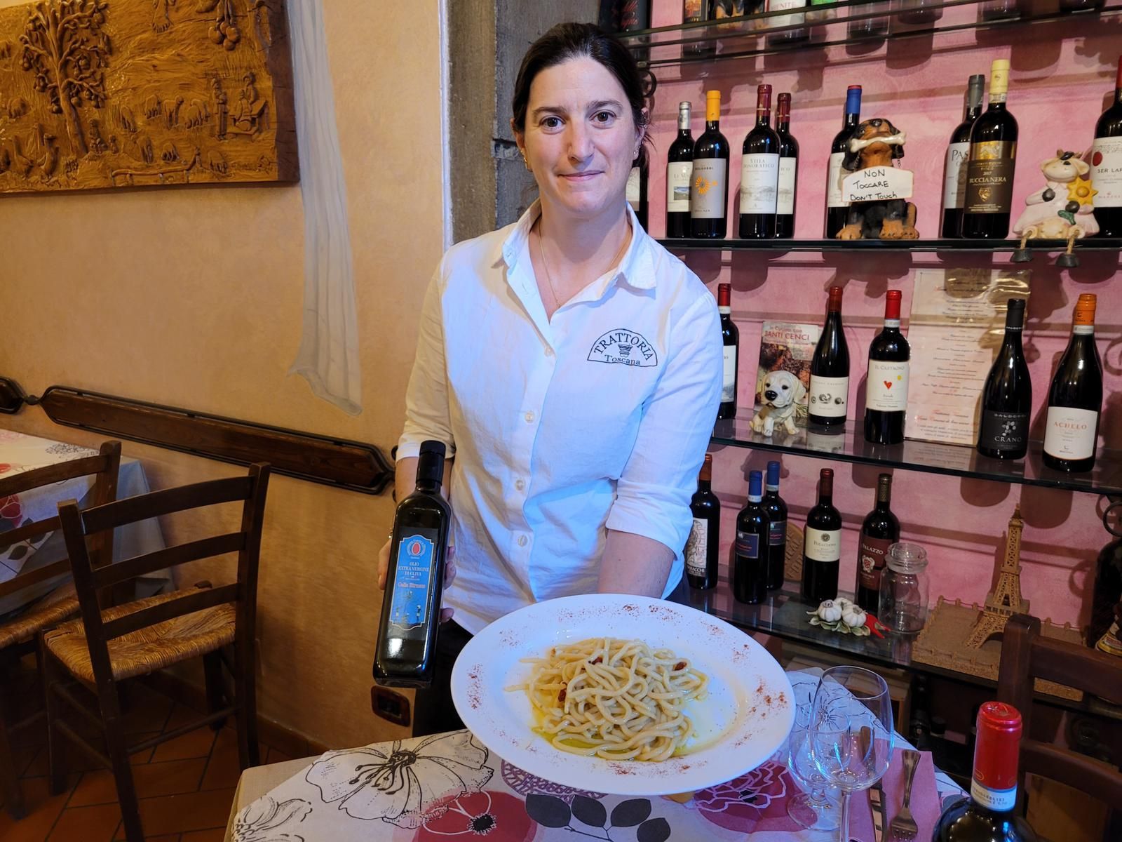 Una donna tiene in mano una bottiglia di vino e un piatto di pasta.