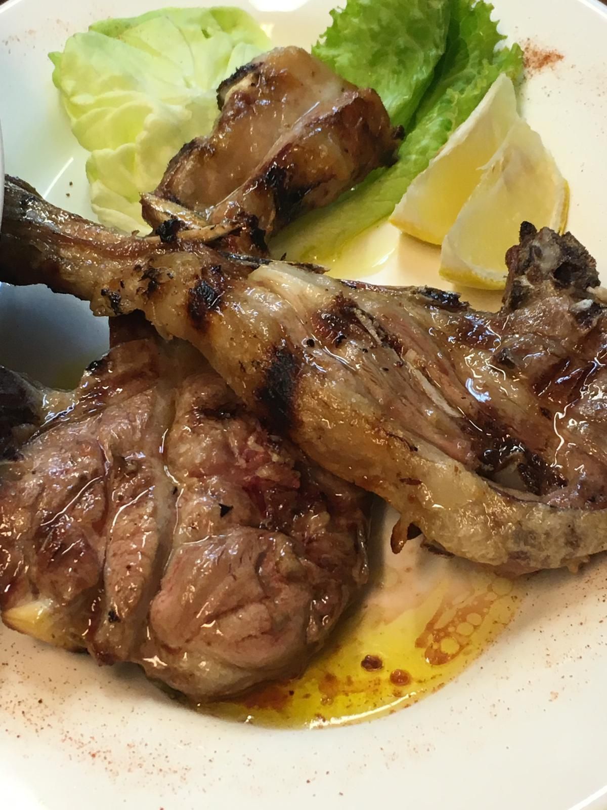 Un piatto bianco con sopra carne, lattuga e fette di limone.