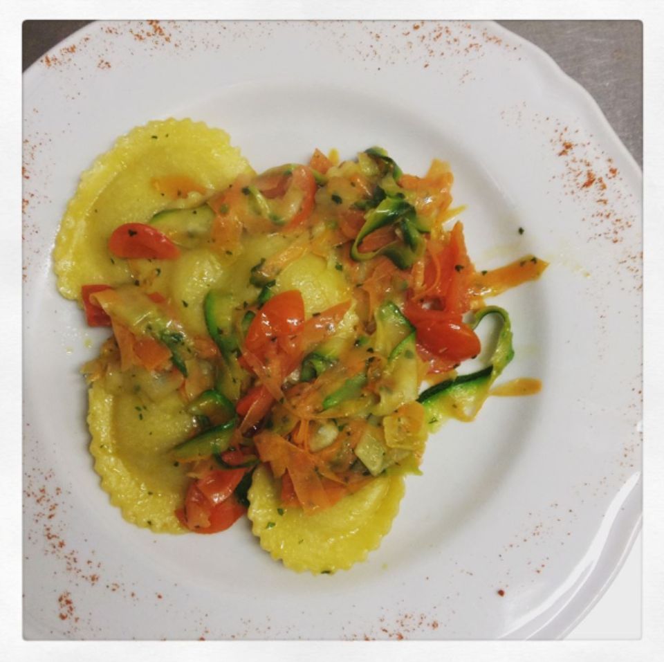 Un piatto bianco condito con ravioli e verdure