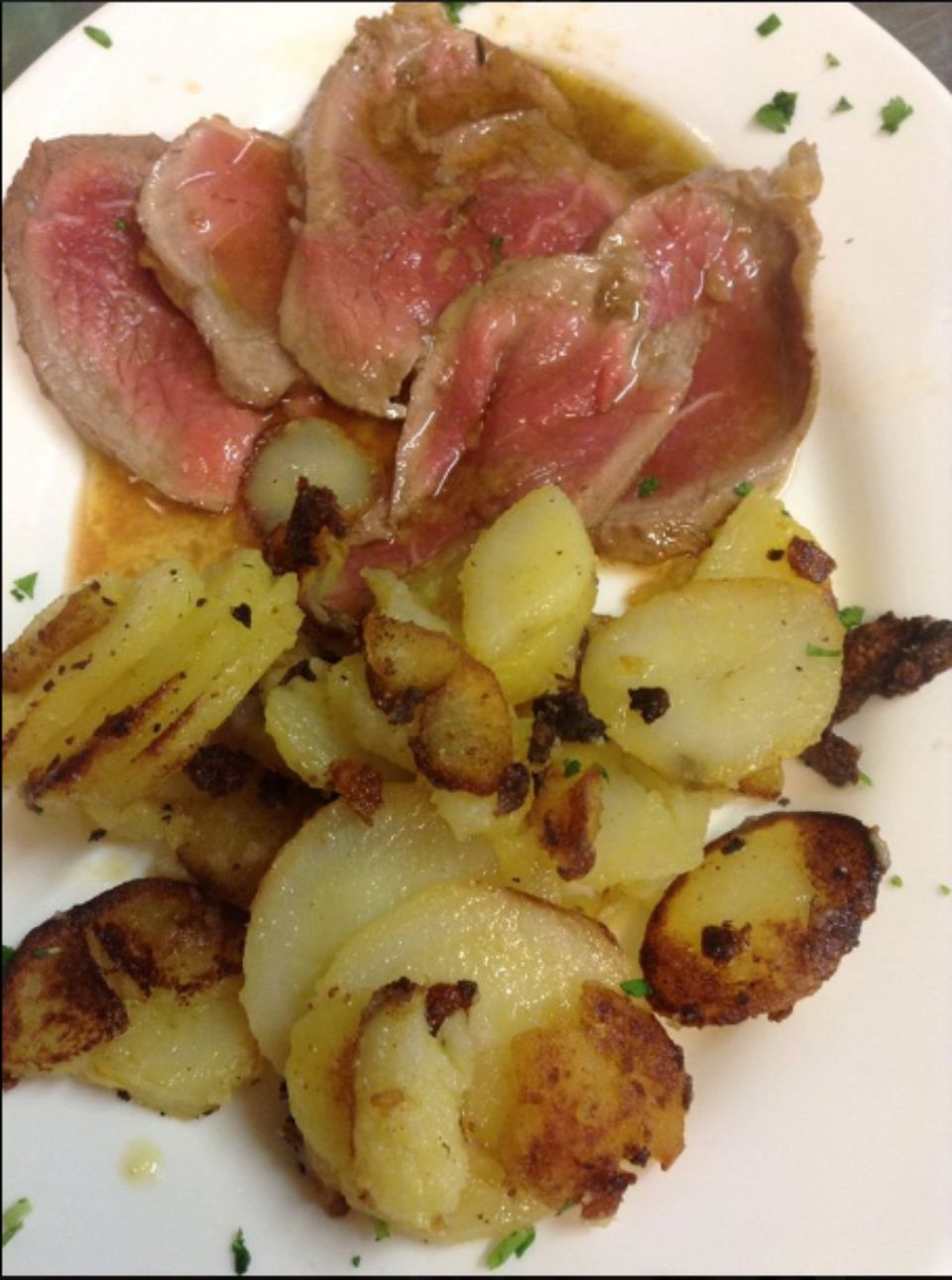 Un piatto bianco con sopra carne e patate