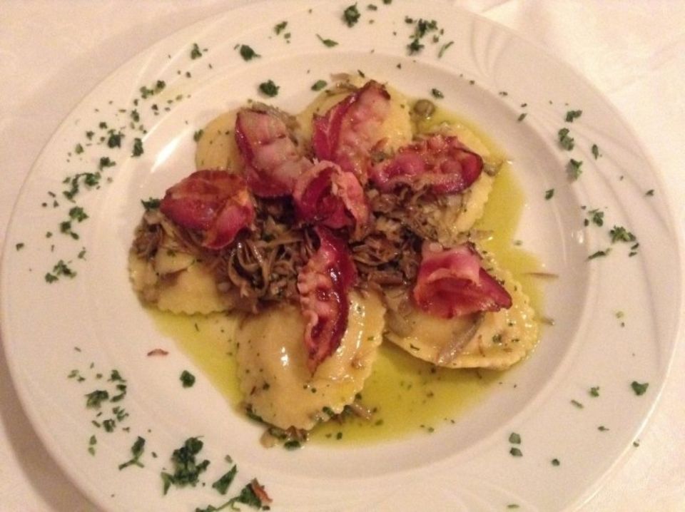 Un piatto bianco con ravioli e pancetta su un tavolo