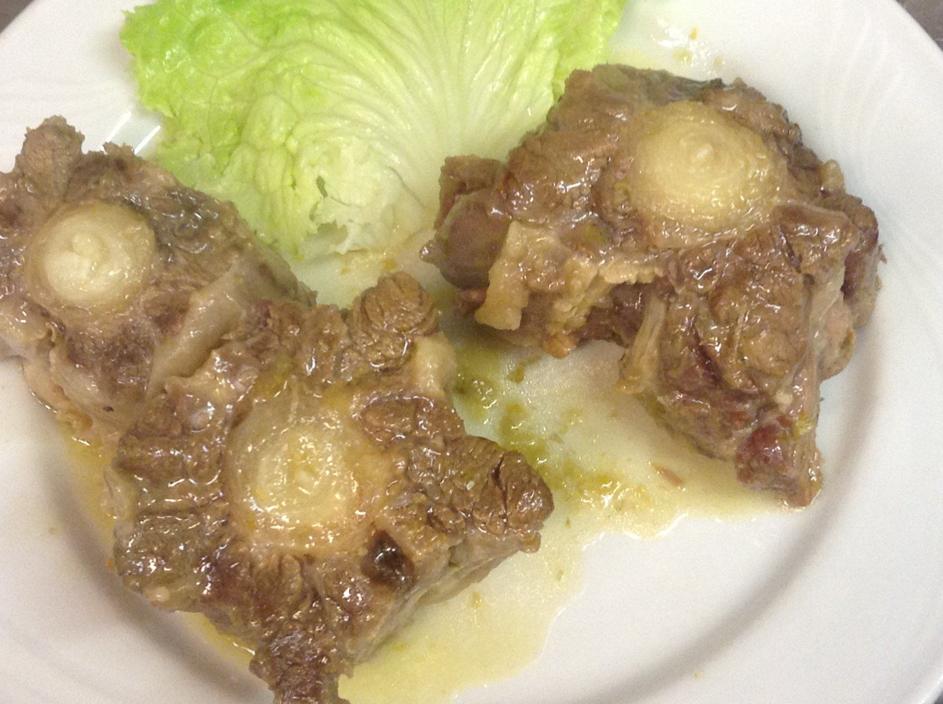 Un piatto bianco con sopra carne e lattuga su un tavolo.