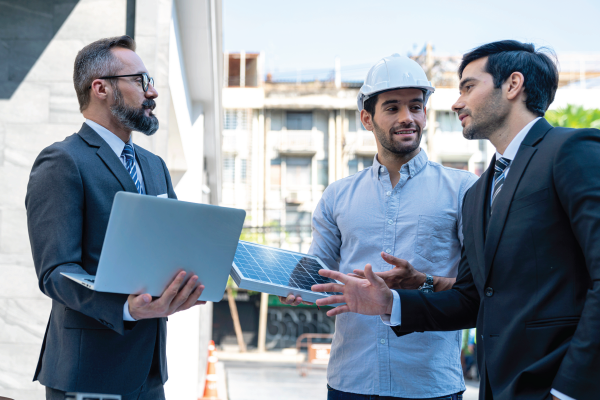 A group of men are standing next to each other and talking . one of the men is holding a laptop.