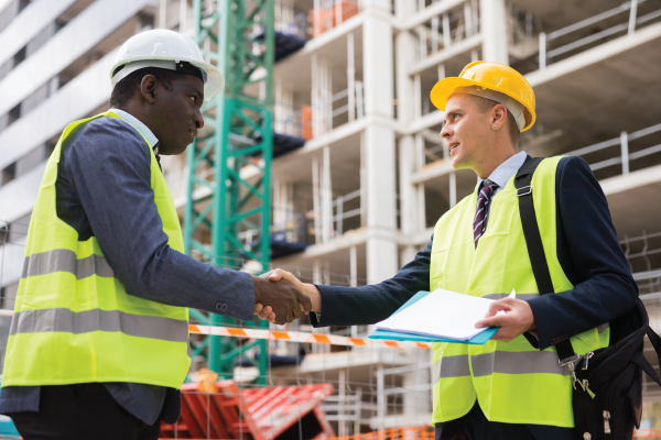 Two construction workers are shaking hands on a construction site.