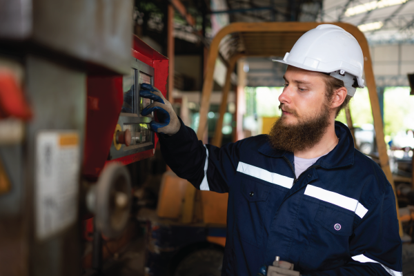 A man in a hard hat is working on a machine in a factory.