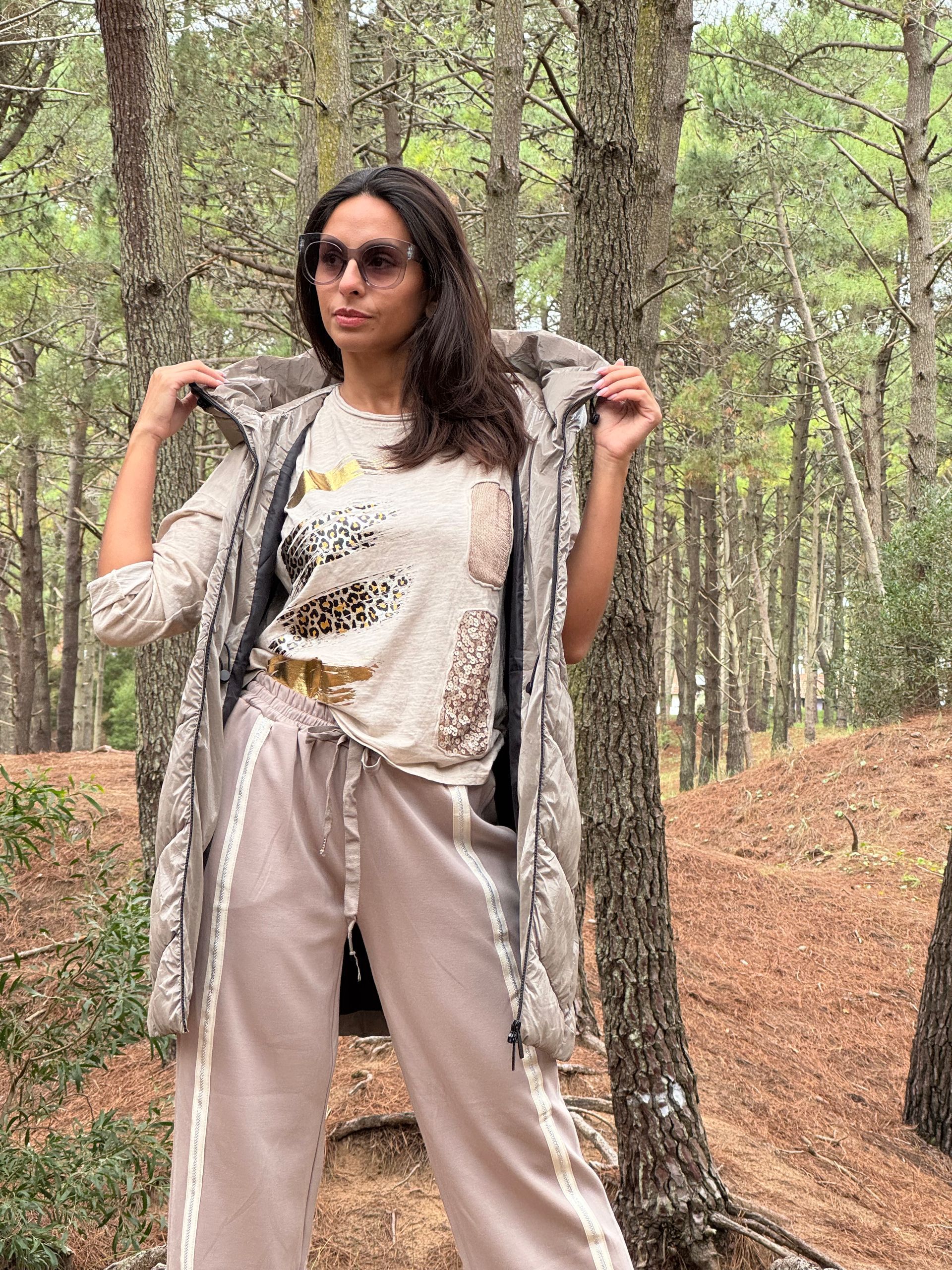 Mujer con abrigo y gafas junto a un árbol en un bosque.