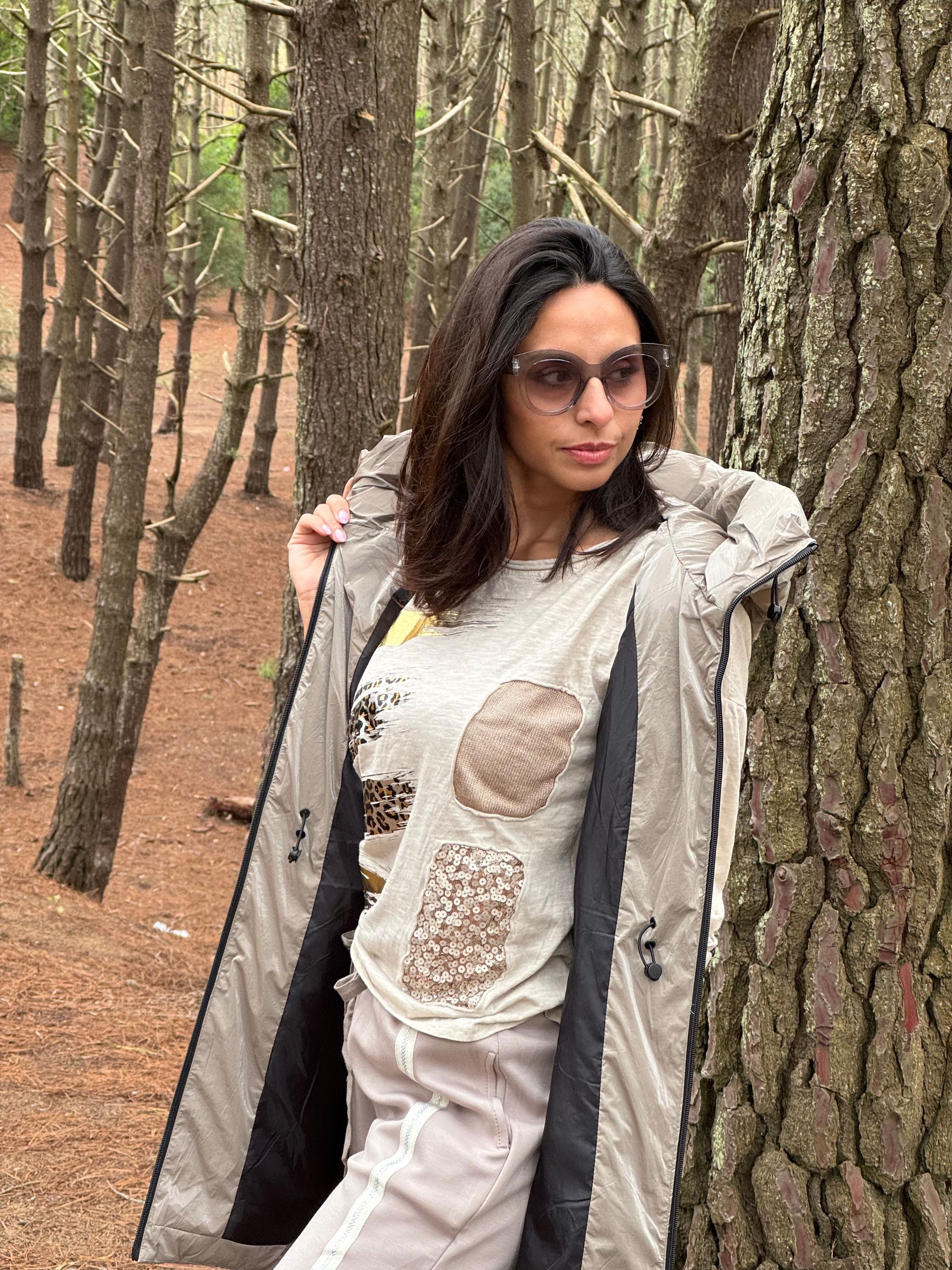 Mujer con abrigo y gafas junto a un árbol en un bosque.