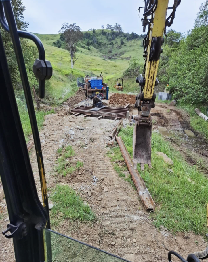 A Yellow and Blue Excavator is Digging a Hole in the Dirt — Barrington Coast Contracting in Minimbah, NSW