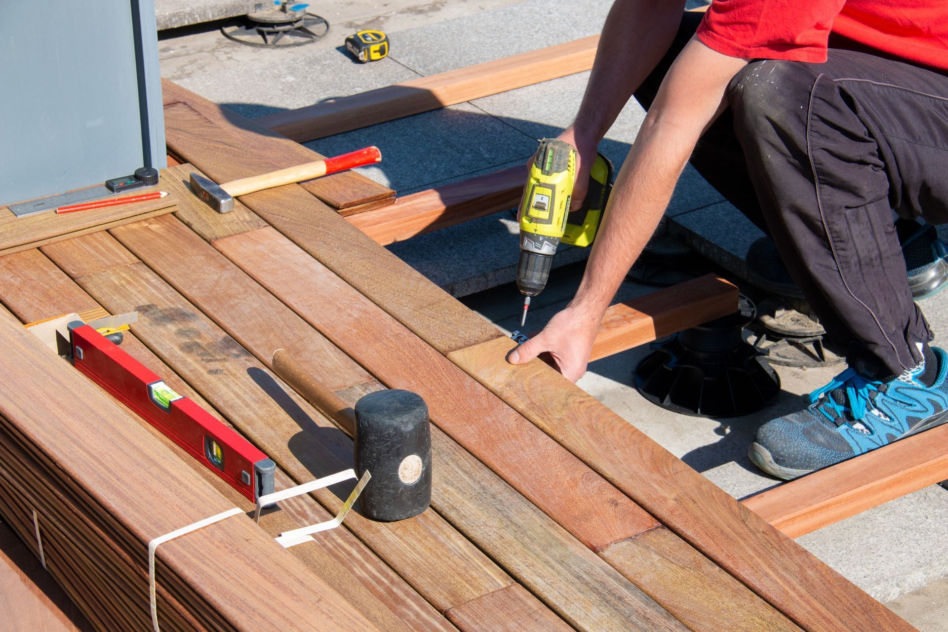 Person using a drill to install wooden deck boards, outdoors.