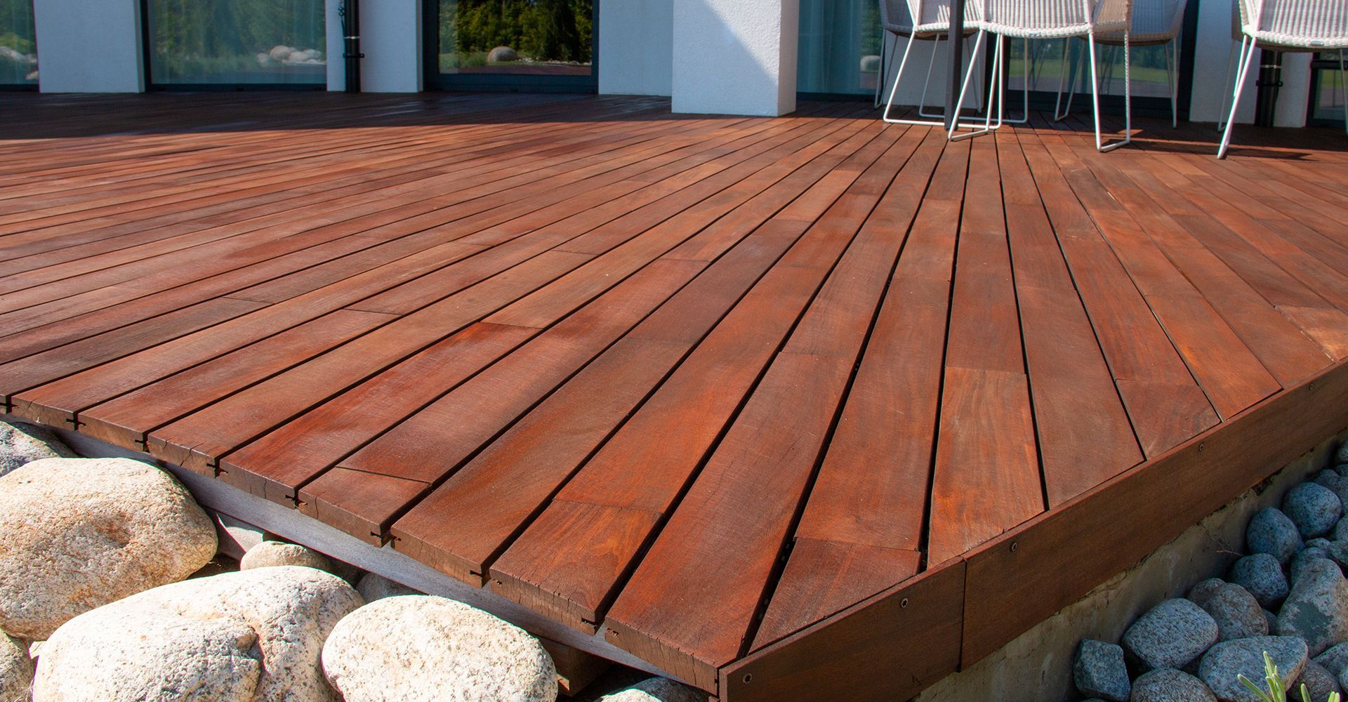 Wooden deck with reddish-brown planks, framed by a metal edge and stones.