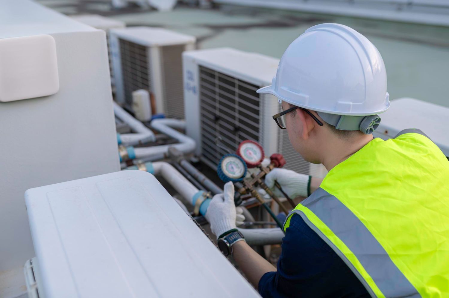 HVAC technician in hard hat and safety vest, working on rooftop air conditioning units.
