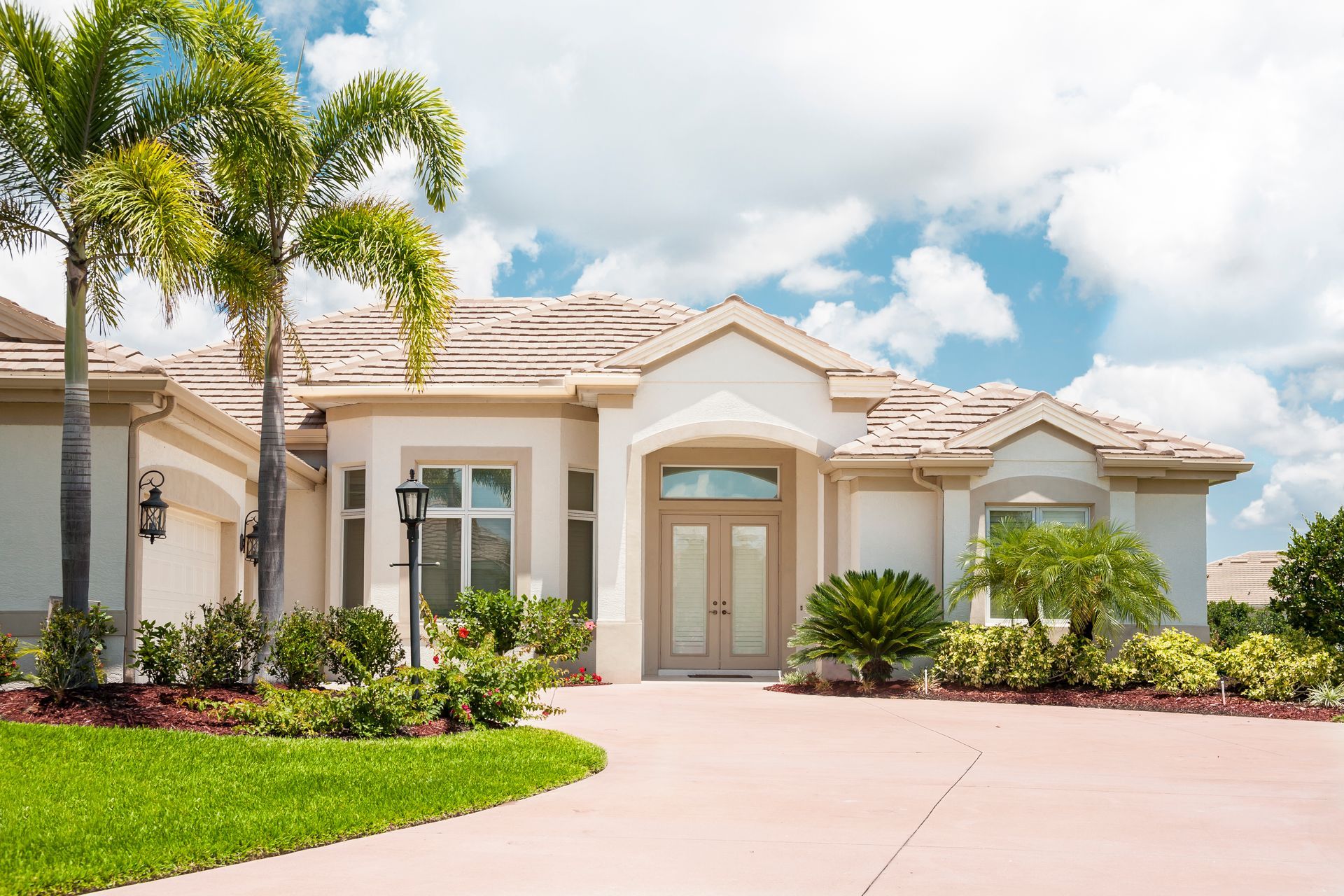 A large white house with a driveway and palm trees in front of it.