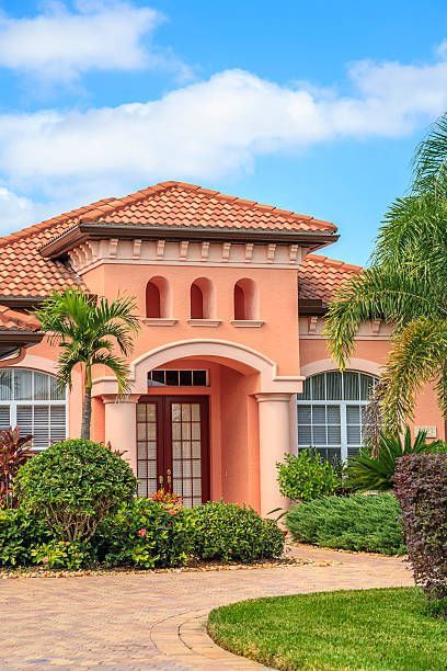 A large pink house with a tile roof and palm trees in front of it.