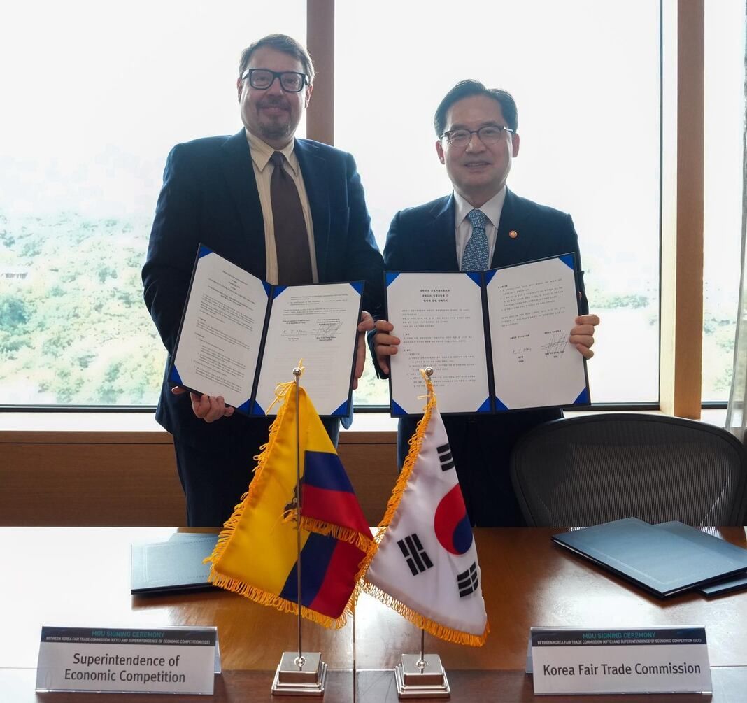 Dos profesionales sostienen documentos firmados frente a las banderas de Colombia y Corea del Sur.