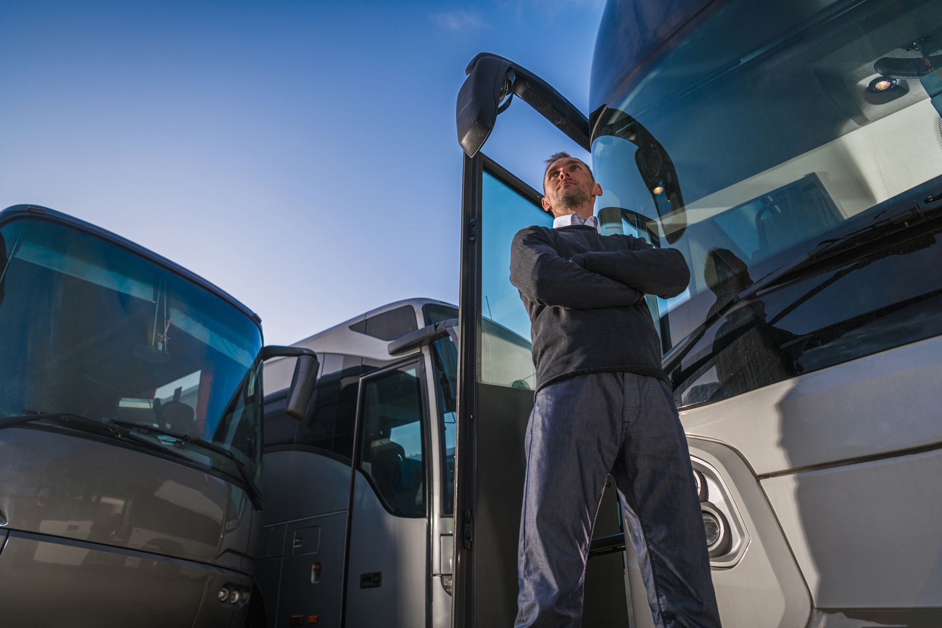 Man standing with arms crossed by parked buses