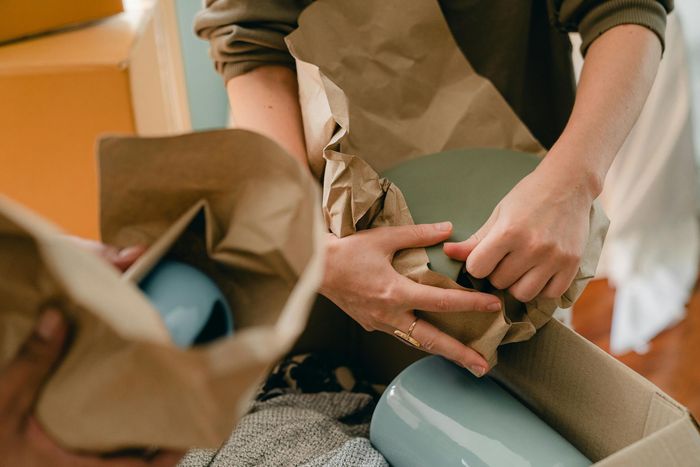 A person is wrapping a vase in brown paper.