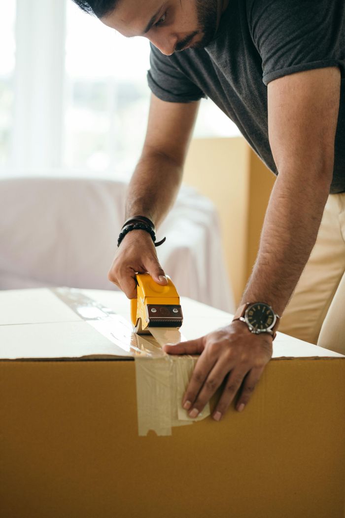 A man is taping a cardboard box with tape.