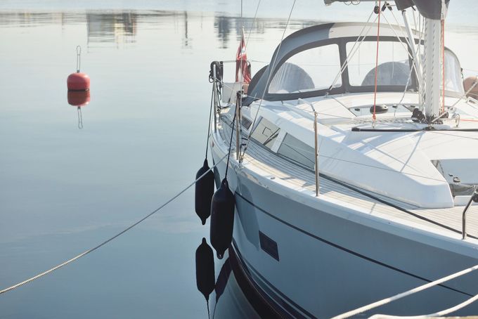 Barca a vela bianca ormeggiata in acque calme accanto a una boa rossa, con parabordi di corda lungo lo scafo.