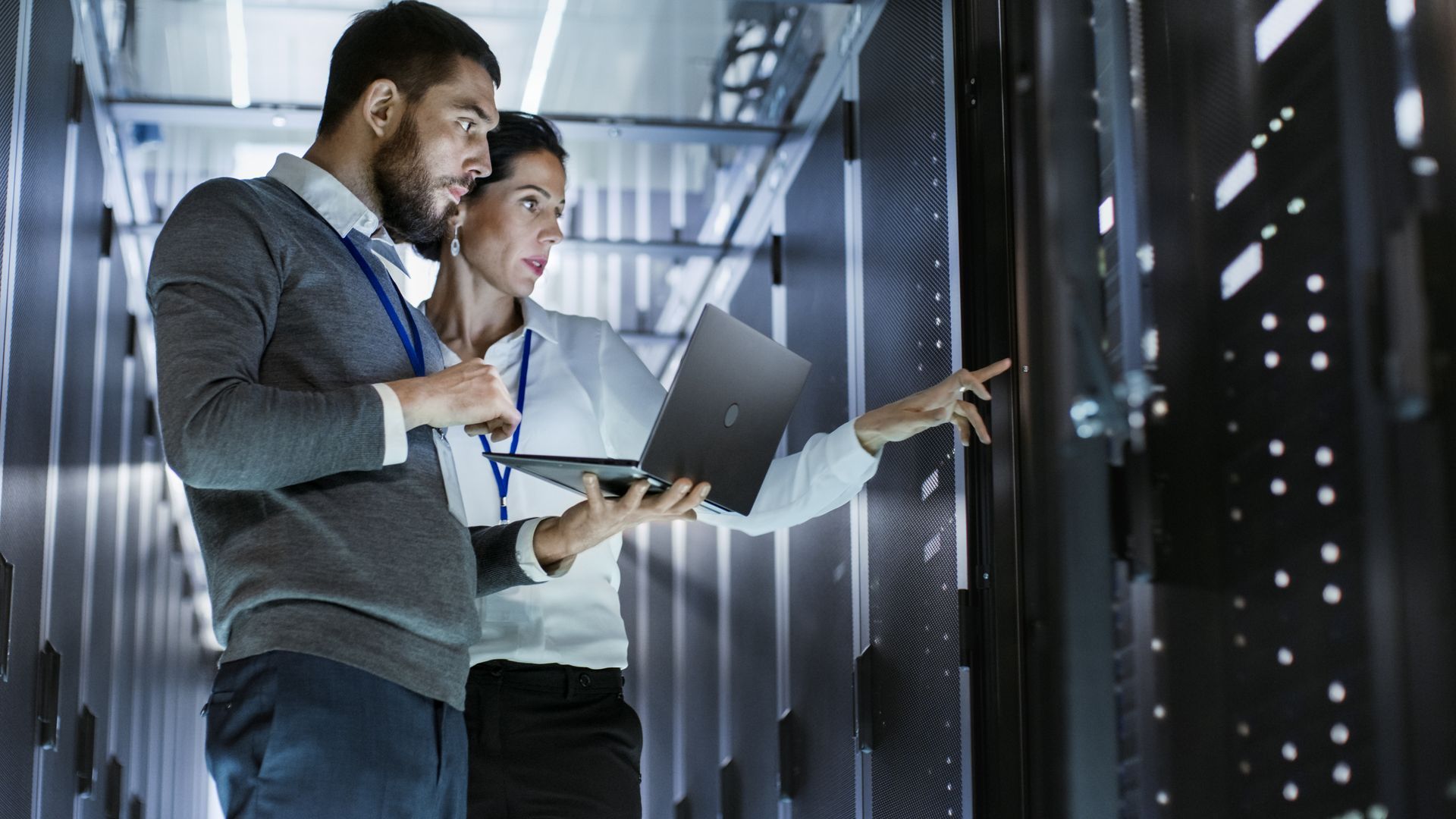 A man and a woman are looking at a laptop in a server room.