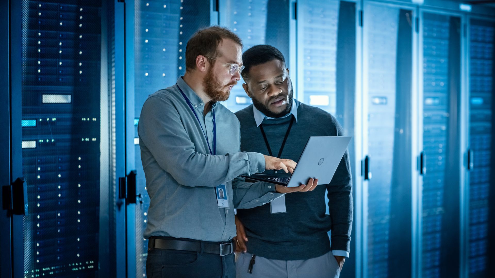 Two men are looking at a laptop in a server room.