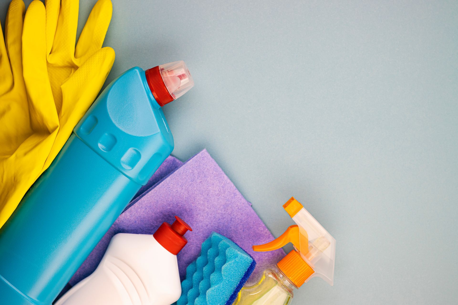 A bottle of cleaning supplies , gloves , sponges , and spray bottles on a table.