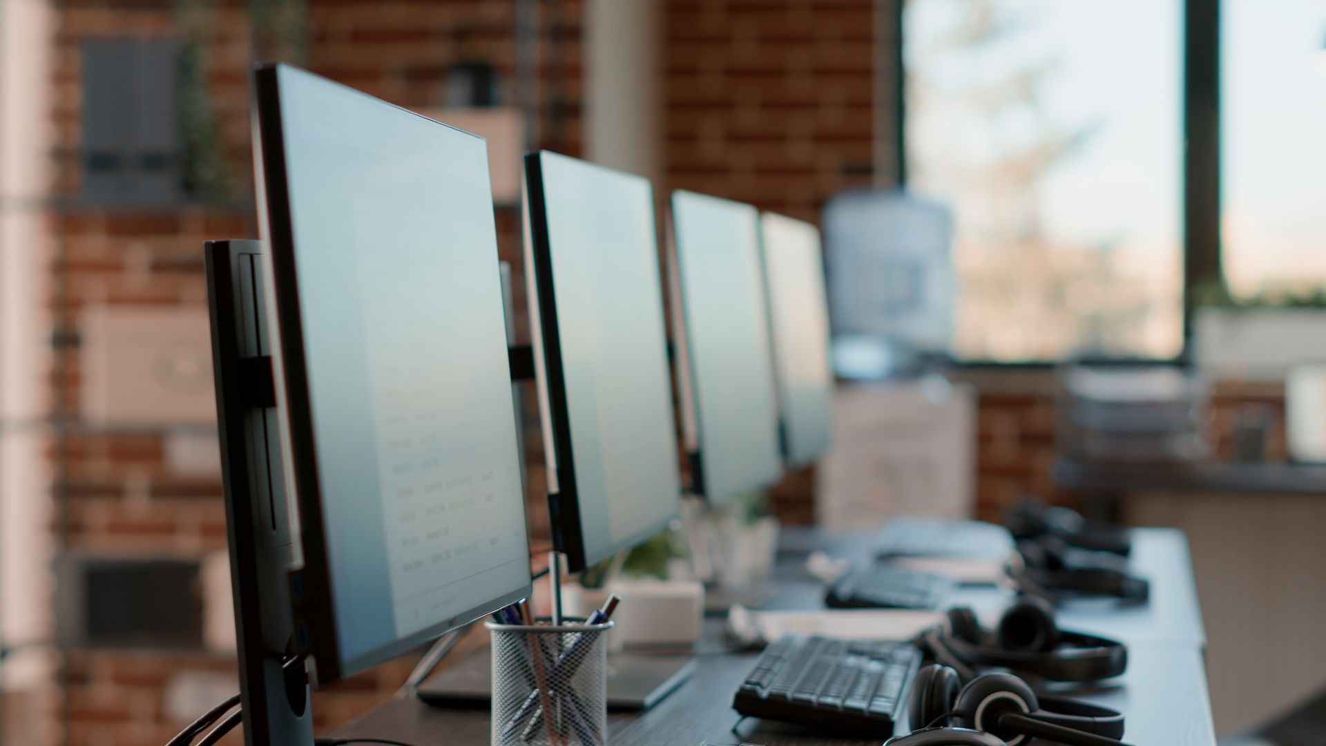 A row of computer monitors sitting on top of a desk in an office.