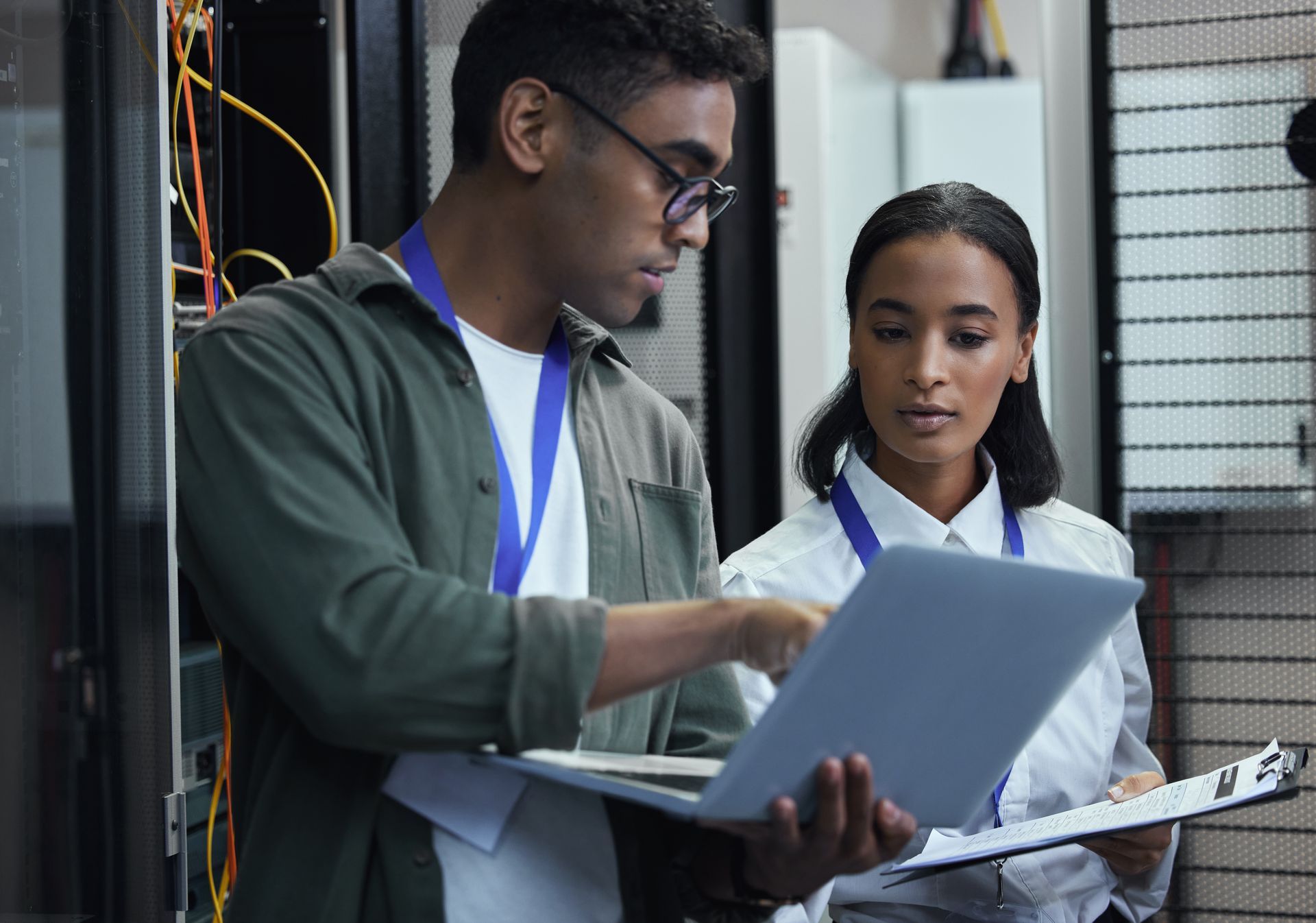 A man and a woman are looking at a laptop in a server room.