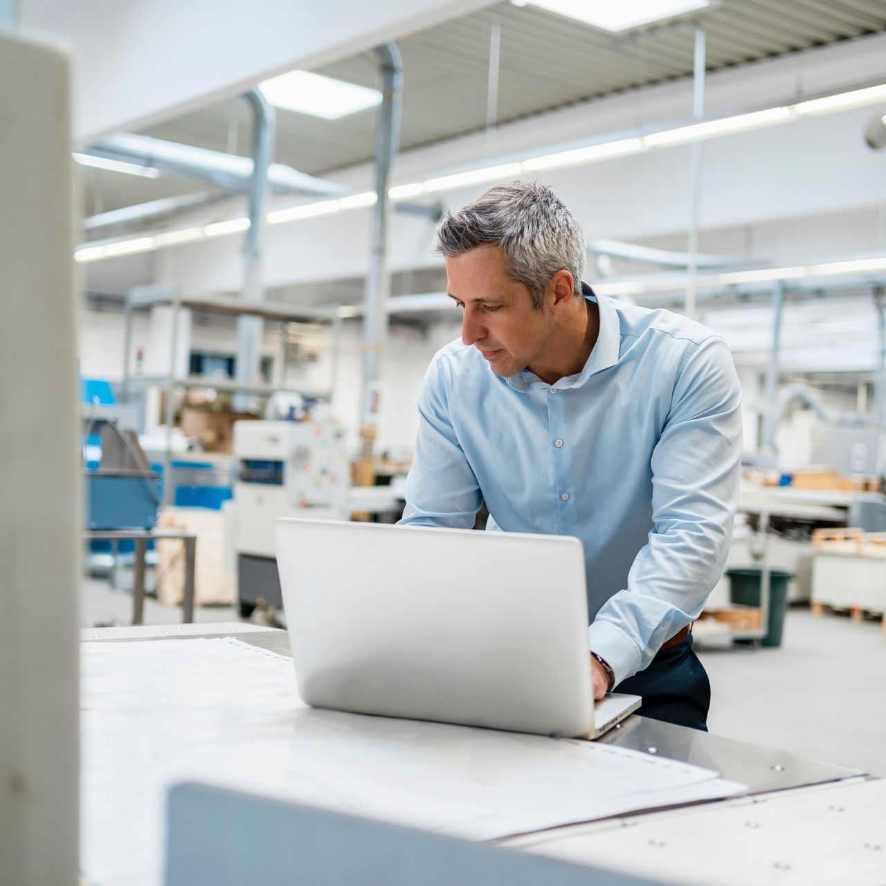 A man is using a laptop computer in a factory.