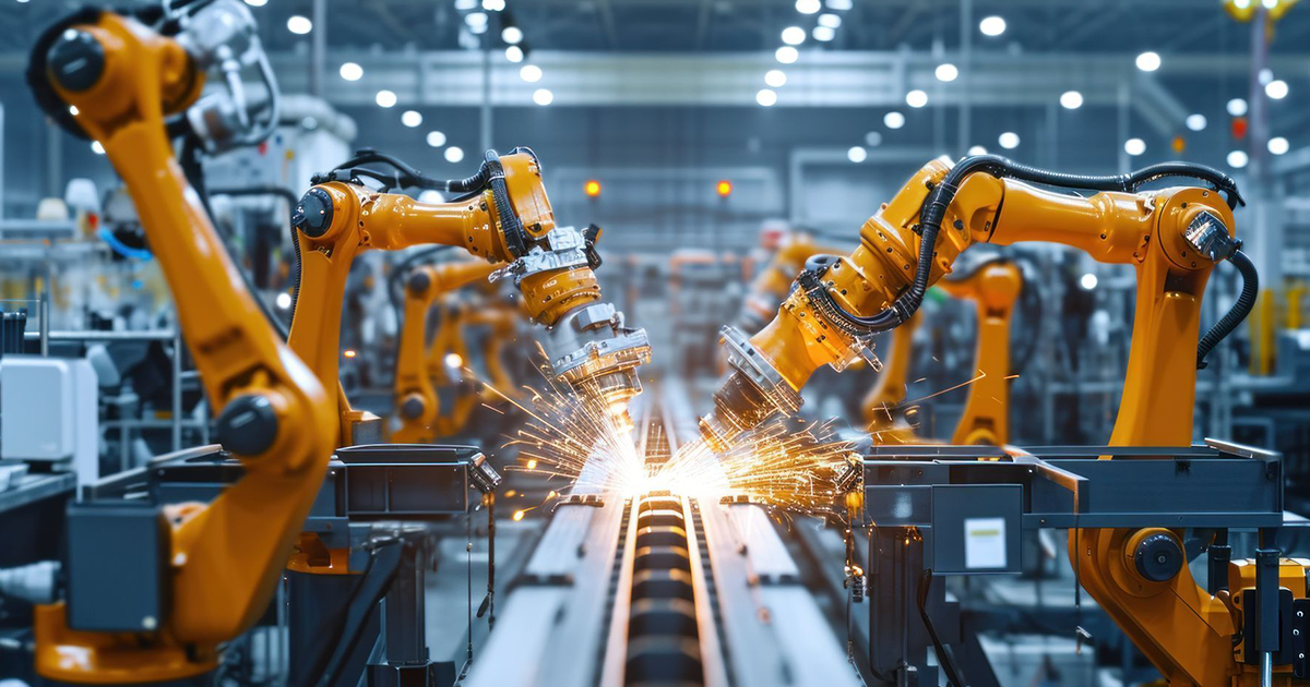 A row of robotic arms are welding a piece of metal in a factory.