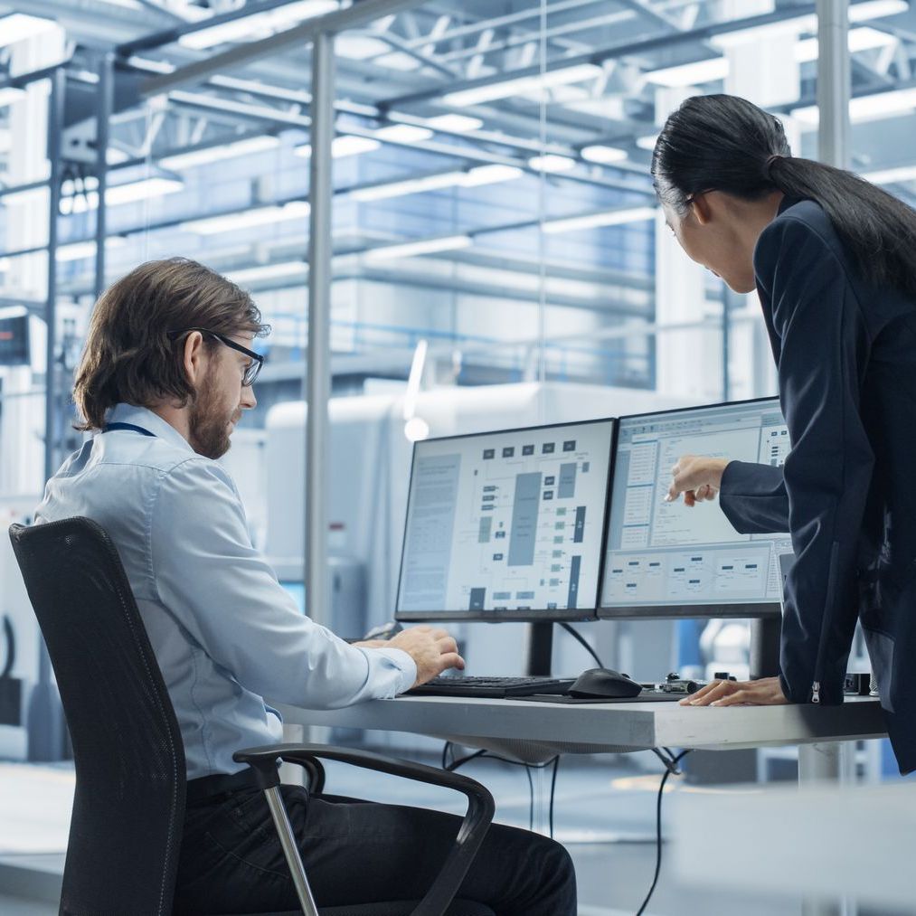 A man and a woman are looking at a computer screen in a factory.