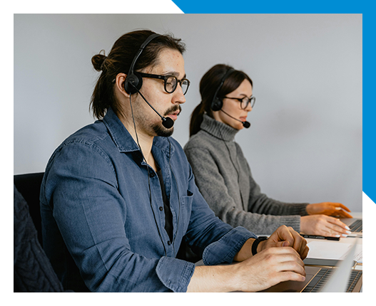 Two people wearing headsets typing on laptops in an office.