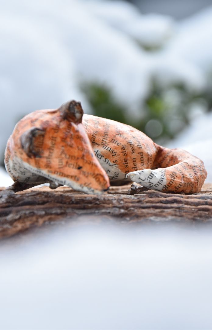Een sculptuur van een vos die op een tak in de sneeuw ligt.