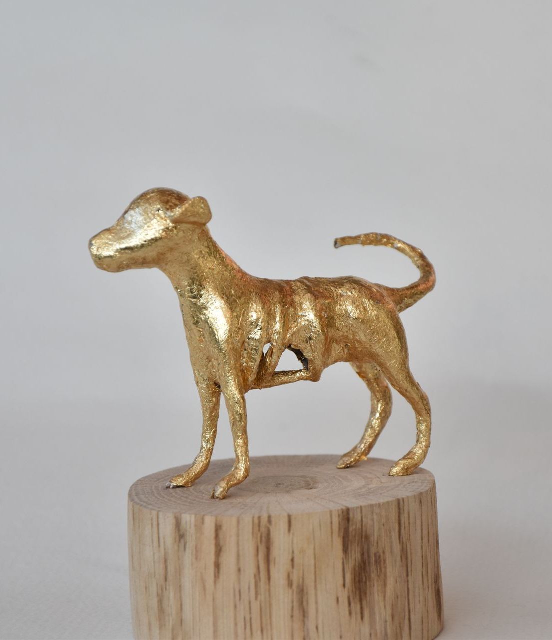 Een gouden beeld van een hond staand op een houten stronk