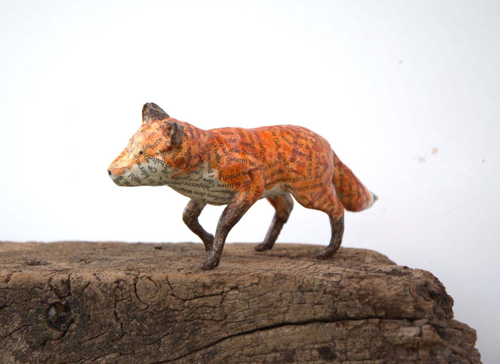 Een standbeeld van een vos die bovenop een stuk hout staat.