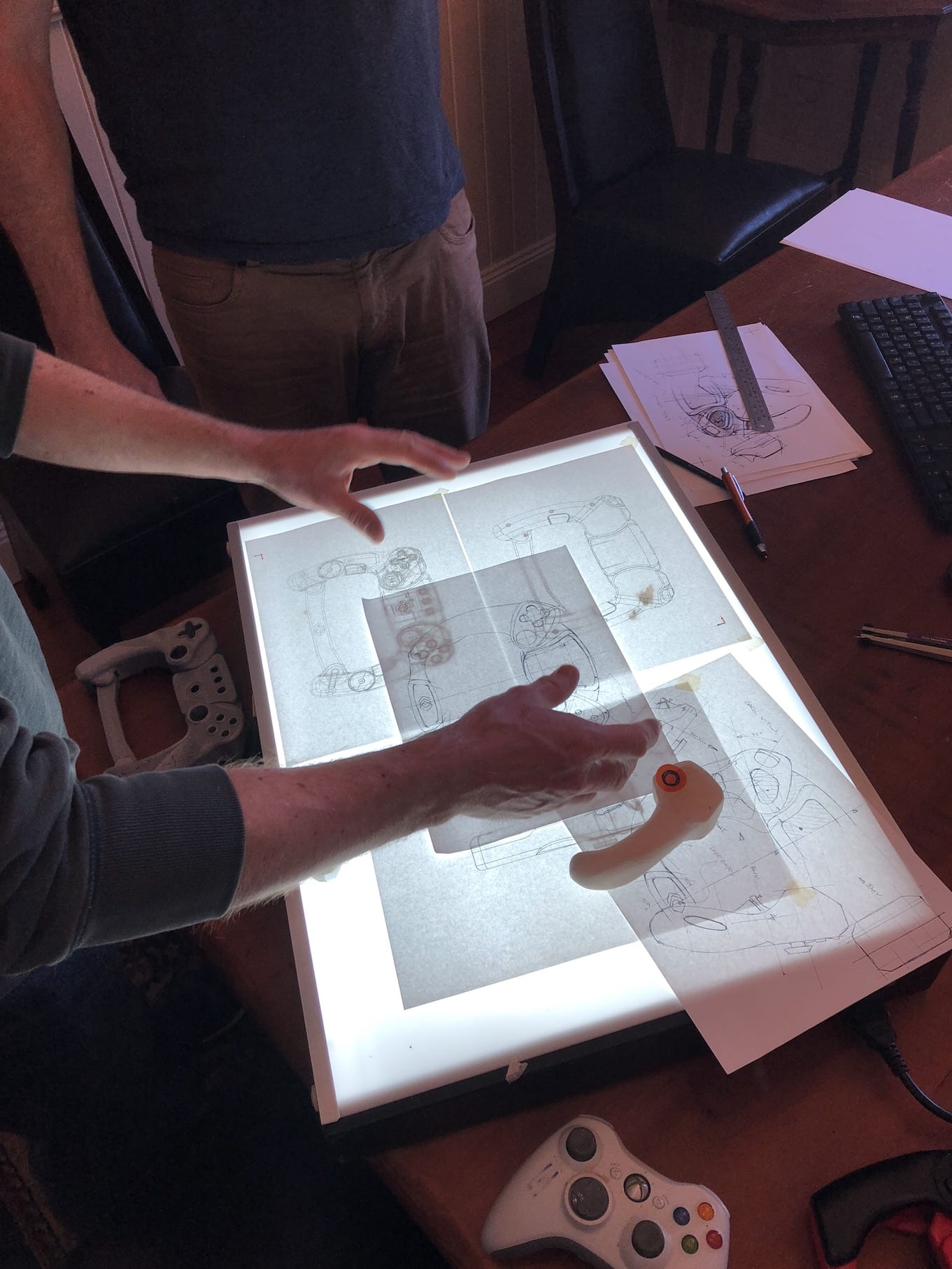 Two people are using a light box to draw on a piece of paper.