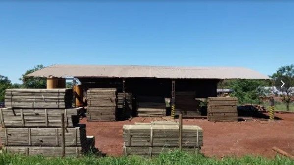 Almacén de madera con leña apilada frente a un cobertizo cubierto, bajo un cielo azul.