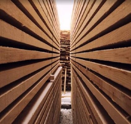 Tablones de madera apilados, luz que se filtra a través de un pasillo estrecho, vista en perspectiva.